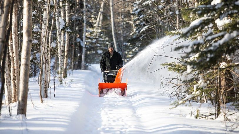 Mann med snøfreser går langs skogsvei