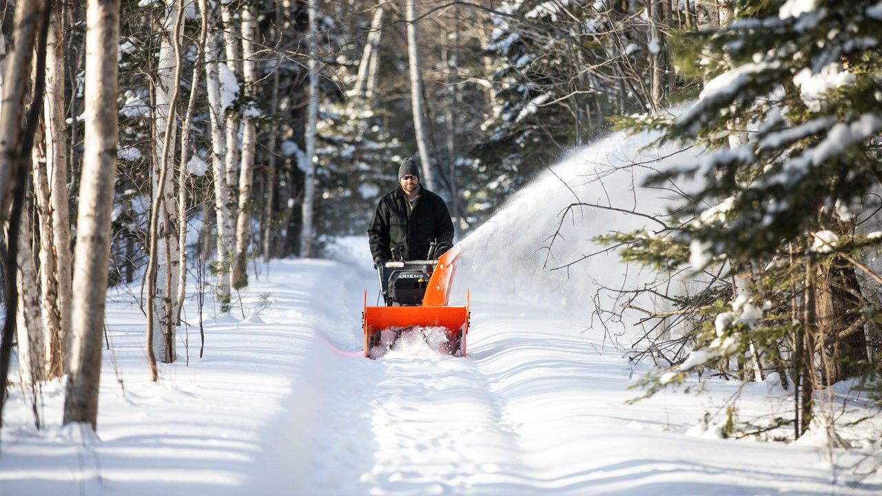 Mann med snøfreser går langs skogsvei